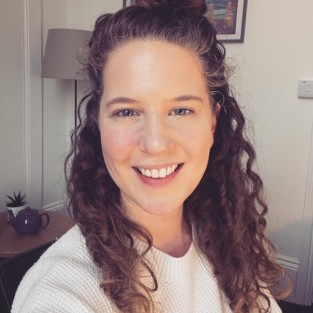 A white woman with long brown curly hair smiles for the camera